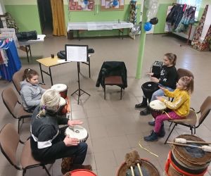 Zdjęcie przedstawia dzieci i instruktora w trakcie nauki gry na bębnach.