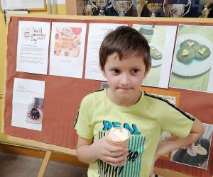 Uczeń stoi przy tablicy z przepisami na desery z nutelli i trzyma kubek z gorącą czekoladą