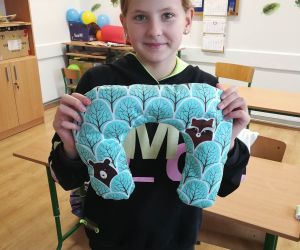 Dziewczynka prezentuje uszytą na maszynie poduszkę podróżną 