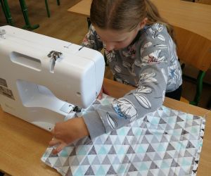 Dziewczynka zszywa materiał na maszynie