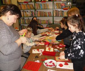 Zdjęcie przedstawia dzieci i dorosłych wykonujących kartki walentynkowe.