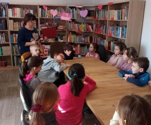 Zdjęcie przedstawia grupę dzieci w trakcie lekcji bibliotecznej.