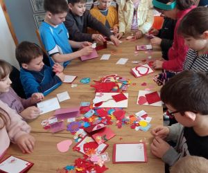 Zdjęcie przedstawia grupę dzieci wykonujących kartki walentynkowe.