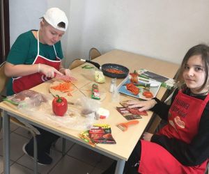 Uczeń kroi marchew, a uczennica siedzi przy stoliku