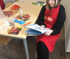 Uczennica w fartuchu kucharskim siedzi i czyta przepis