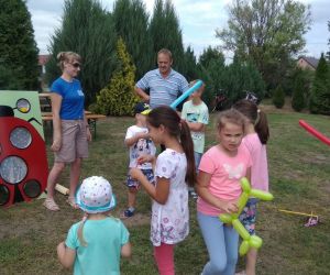 Dzieci bawią się na dworze podczas festynu. Dziewczynka rzuca piłką w zabawkę biedronkę.