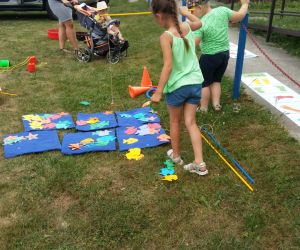 Na zdjęciu dwoje dzieci za pomocą specjalnej wędki zakończonej magnesem łowią zabawkowe rybki. Dzieci bawią się na dworze.