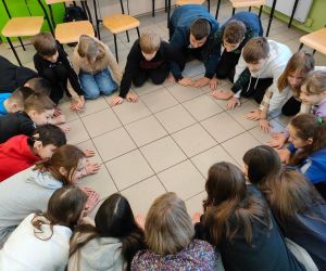 Grupa osób klęczy w kole wewnątrz budynku. Młodzież gra w grę 