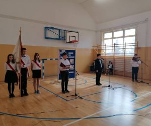 Trzech uczniów stoi przy mikrofonach, obok stoi Poczet sztandarowy