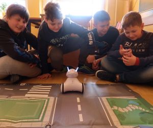 Chłopcy siedzą na podłodze obok maty Smart City i obserwują zachowanie robota.