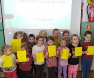 Grupa dzieci stoi przy tablicy interaktywnej. Trzymają w dłoniach żółte kartki.