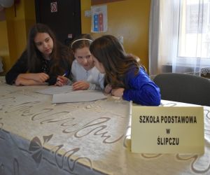 Zdjęcie przedstawia trzy dziewczynki siedzące przy stole nad kartką.