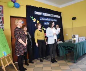 Zdjęcie przedstawia cztery osoby dorosłe, jedna z nich odczytuje wyniki konkursu.