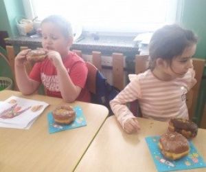 dzieci siedzą przy stole, jedzą pączki