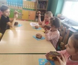 dzieci siedzą przy stole, jedzą pączki