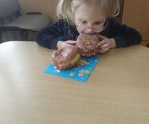 Mała dziewczynka z wielkim apetytem gryzie pączka z lukrem