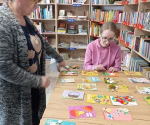 Na zdjęciu widoczne są dwie osoby przeglądające kartki wielkanocne. W tle regały z książkami.