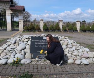 Uczennica składa bukiet żonkili pod tablicą pamiątkową