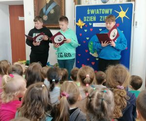 Trzech uczniów stoi przed okazjonalną dekoracją, jeden z nich czyta informacje na temat Światowego Dnia Ziemi