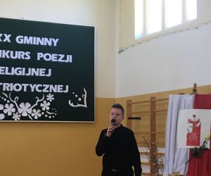 Uczeń w stroju galowym recytuje na tle dekoracji okolicznościowej