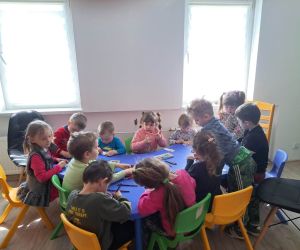 Zdjęcie przedstawia dzieci siedzące przy stoliku.