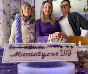 Trzy kobiety pozują do zdjęcia. Na pierwszym planie fioletowy lampion i kosz z wikliny.