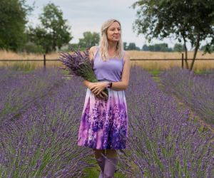 Kobieta w fioletowym ubraniu stoi pomiędzy grządkami lawendy