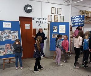 Uczniowie młodszych klas oglądają tablice dekoracyjne oraz transparenty trzymane przez uczniów