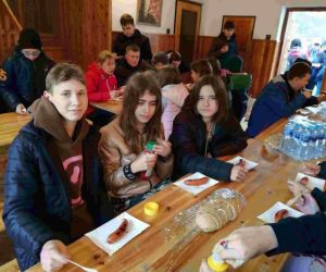 Uczniowie siedzą przy stolikach i jedzą kiełbaski z grilla