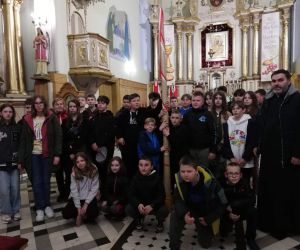 Uczniowie trzymają w dłoniach zabytkową świecę i pozują do wspólnej fotografii z nauczycielami i księdzem na tle ołtarza