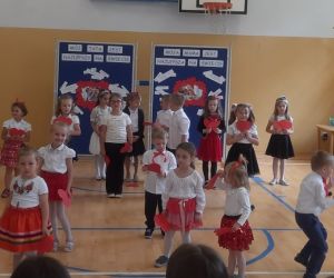 Przedszkolaki w strojach galowych na tle tablicy dekoracyjnej