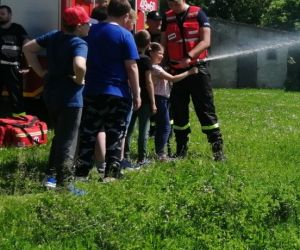 boisko szkolne, uczniowie w asyście strażaka bawią się wężem strażackim
