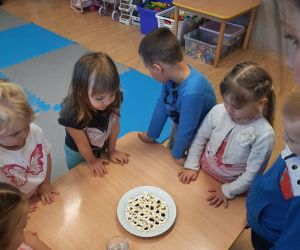 Przedszkolaki dookoła stołu. Na stole talerz i kubek z wodą