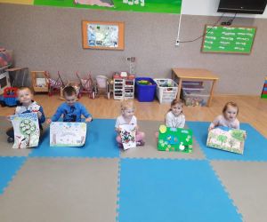 Przedszkolaki siedzą na dywanie i prezentują prace plastyczne z kolorowymi drzewami