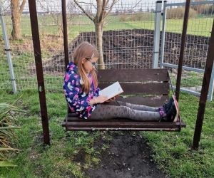 Dziewczynka czytająca książkę na huśtawce na podwórku