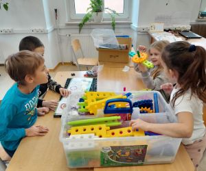 Uczniowie klasy drugiej przy stoliku wyjmują klocki z pudełka