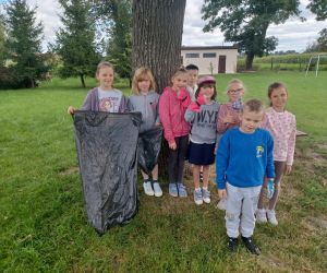 Kilkoro młodszych uczniów stoi przy drzewie z workami na śmieci