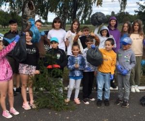 Grupa uczniów stoi przy szkole z workami śmieci