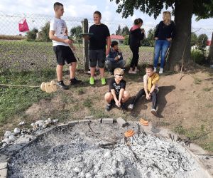 Uczniowie siedzą przy ognisku i pieką kiełbaski