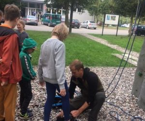 Instruktor zakłada dziewczynce pas zabezpieczający przed wyjściem na ścianę wspinaczkową