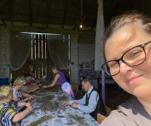 W stodole wielki stół na którym leży wysuszona lawenda, przy nim siedzą ludzie, Prowadząca spotkanie stoi,ubrana jest na fioletowo