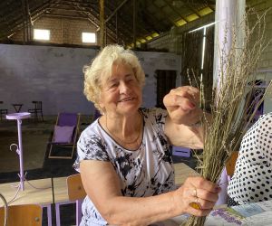 Kobieta trzyma w ręku pęk suchych gałązek lawendy, obwiązuje je nitką,