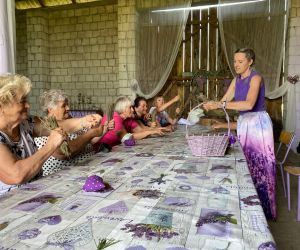 W stodole wielki stół na którym leży wysuszona lawenda, przy nim siedzą ludzie, Prowadząca spotkanie stoi,ubrana jest na fioletowo