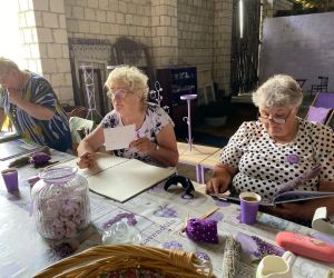 Seniorki przeglądają fioletowe albumy ze zdjęciami, jedna z nich trzyma kartkę w ręku