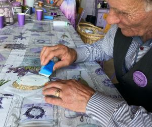 Mężczyzna, uczestnik warsztatów maluje farbami mały plaster drewna