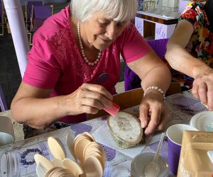 Kobieta, uczestniczka warsztatów maluje farbami mały plaster drewna