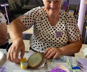 Kobieta, uczestniczka warsztatów maluje farbami mały plaster drewna