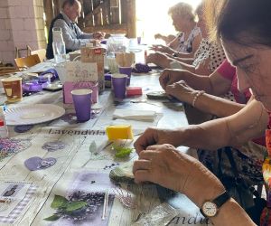 Seniorzy siedzą przy stole, są zajęci wykonywaniem pracy plastycznej