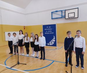 Grupa uczniów klasy trzeciej w strojach galowych przy mikrofonach