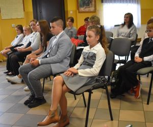 Zdjęcie przedstawia młodzież i dorosłych słuchających recytacji.